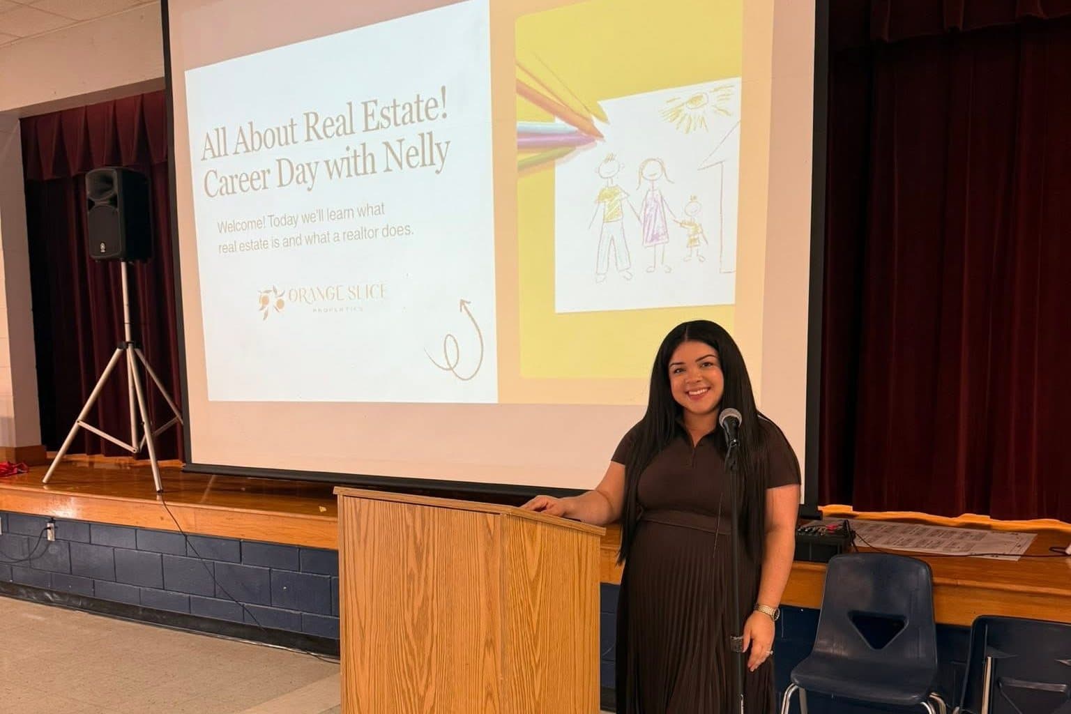 Nelly at the podium in a school auditorium under a slide that reads "All About Real Estate, Career Day with Nelly"