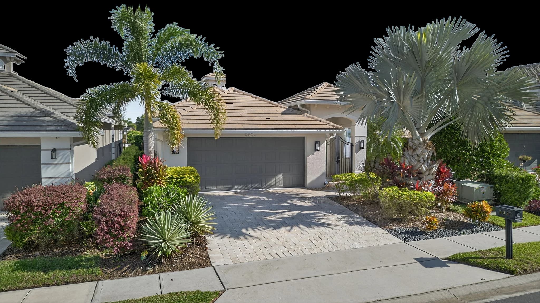 A single-story Providence home with a tile roof, a foxtail palm and a silver Bismarck palm, and bright tropical landscaping
