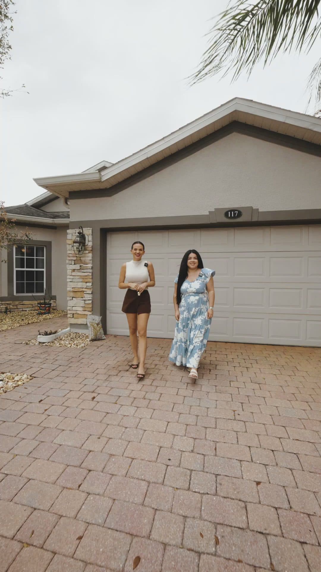 Luana and Nelly walk down the driveway of 117 Preston Ave in front of the two-car garage, a still from the video tour