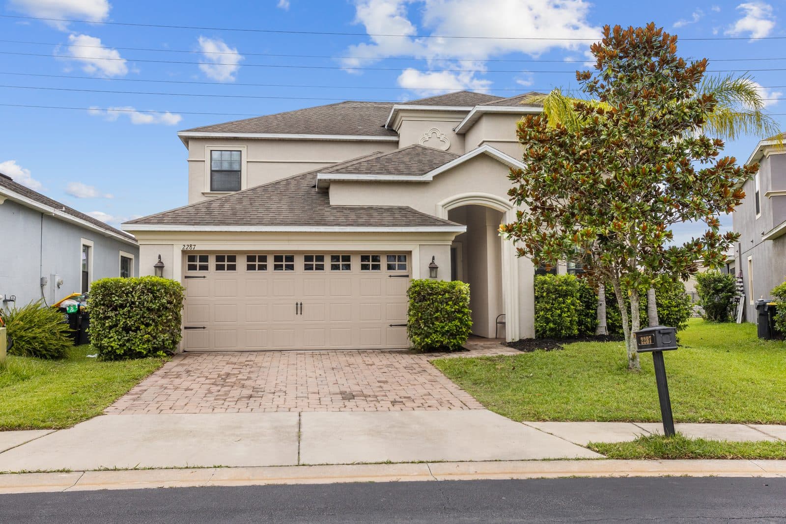 Front of 2287 Victoria Dr, a two-story home with an arched entry, a two-car garage, and a magnolia tree in the front yard