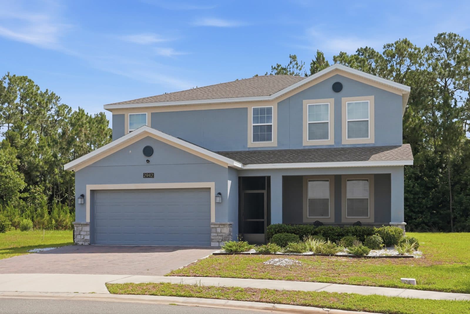 Front of 2942 Camden Way, a two-story home with stone accents, a paver driveway, a screened front porch, and pine trees behind