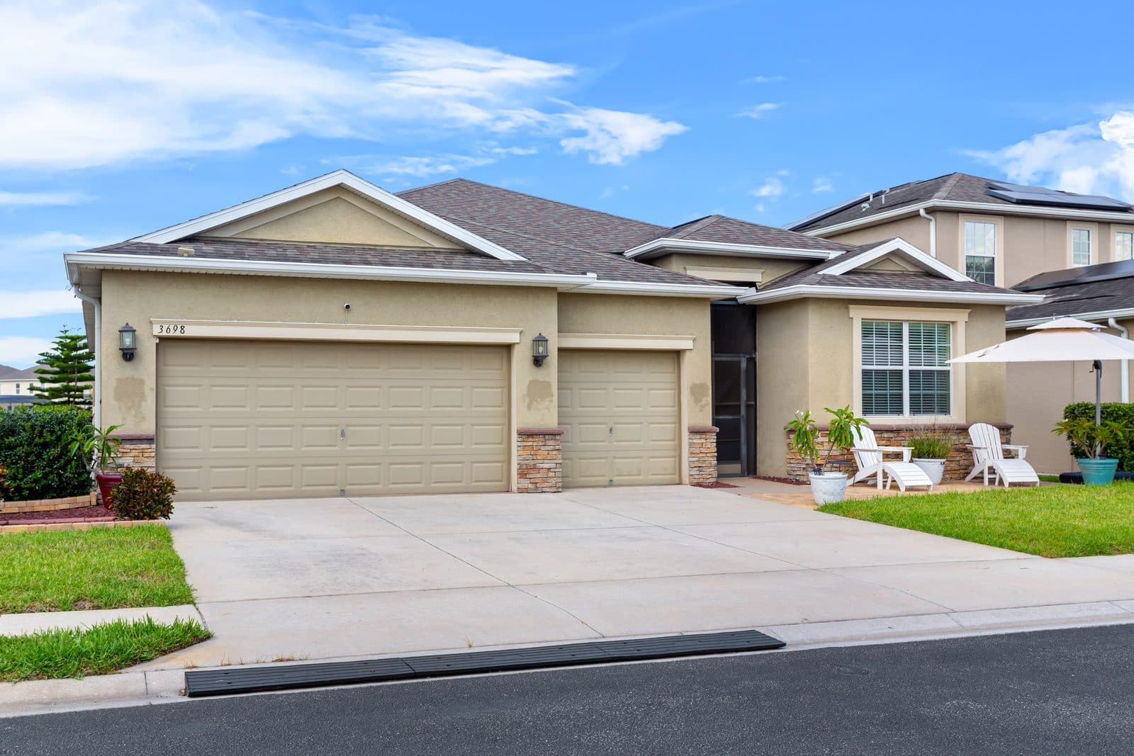 Front of 3698 Cortland Dr, a single-story home with a three-car garage, stone accents, and a front patio with white Adirondack chairs