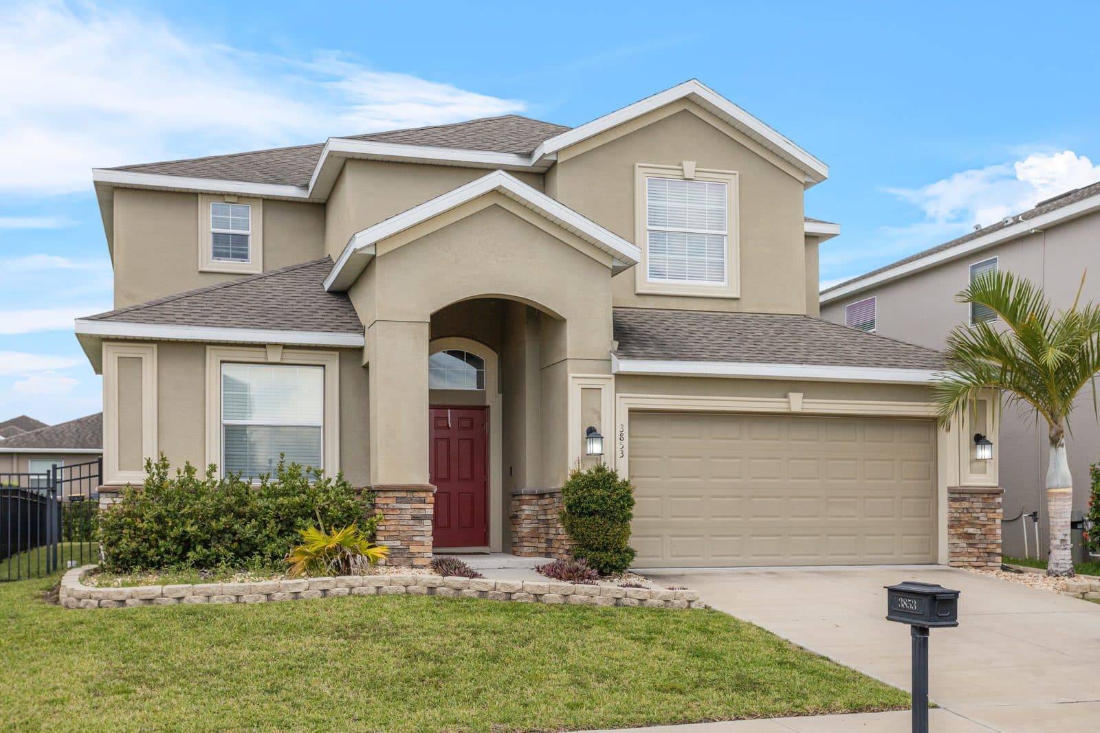 Front of 3853 Cortland Dr, a two-story home with a red front door, stone accents, a wide garage door, and a palm tree