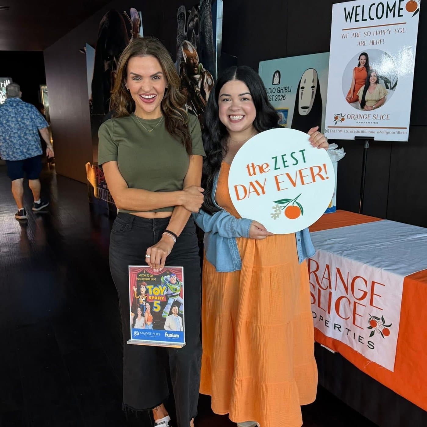 Luana and Nelly at the theater entrance with a Toy Story 5 flyer and an Orange Slice sign that says "The zest day ever"